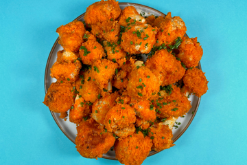 A blue plate with buffalo hot sauce covered cauliflower wings, with a side of Ranch Mayo as a dip on the side.