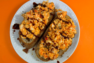 a white plate with sourdough bread and scrambled eggs on top, topped with spicy breakfast sauce.