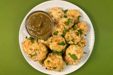 A plate of Cauliflower cheese bites, on a green background, with a side of Brussels Sprout Ketchup on the plate.