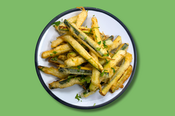 A white plate with crispy courgette (zucchini) fries on top, the fries have chopped coriander on top and hot sauce in the batter