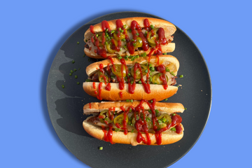 A plate of three hot dogs that are topped with bbq chilli, cheese, jalapeno, and Honey Chipotle BBQ Sauce