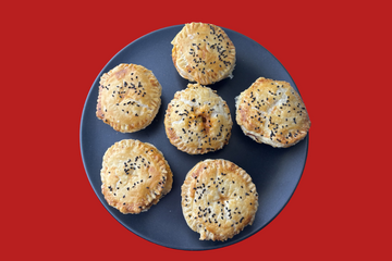 A black plate with chicken pies on top that are covered in black seeds and filled with a buffalo chicken mixture.