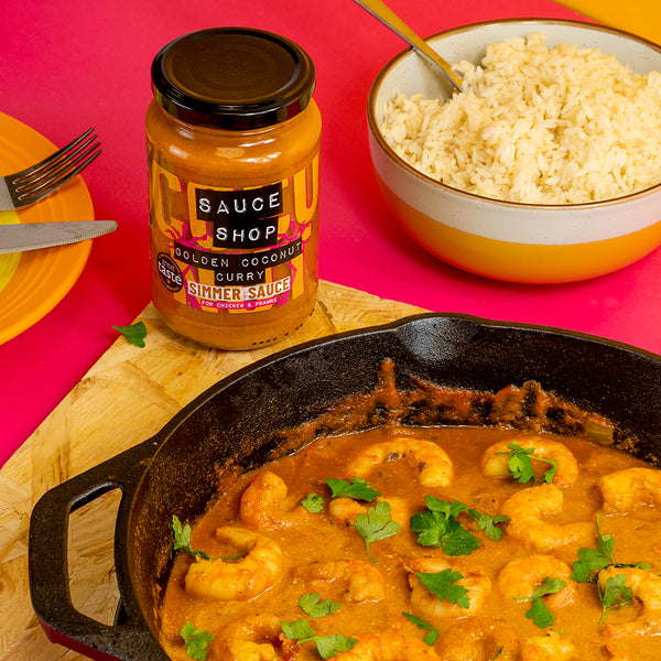 A jar of Sauce Shop Golden Coconut Simmer Sauce with a bowl of rice and prawn curry on a pink background