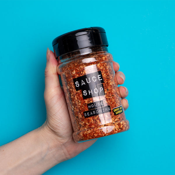 A shaker jar of Sauce Shop House Seasoning being held up against a cyan background