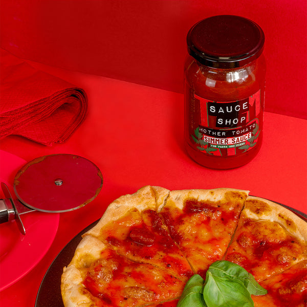 A jar of Sauce Shop Mother Tomato next to a pizza with fresh basil on top