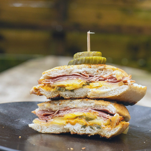 A sandwich with Sauce Shop Mustard and ham inside and pickles on top